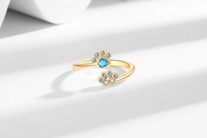 Detailed macro of golden pet paw ring featuring blue heart zircon and crystal settings