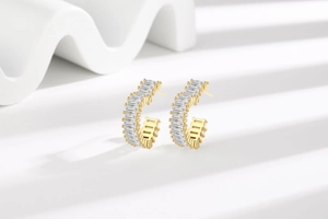Detailed macro view of gold-plated C-shape earrings with baguette-cut zircon inlays