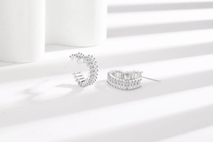 Detail of silver C-shaped stud earrings with rows of rectangular clear zircon stones