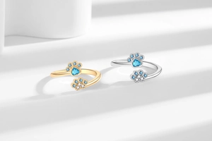 Detail of adjustable paw print rings with blue heart stones in gold and silver finish