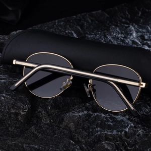 Detailed close-up of retro oval gold metal sunglasses resting on black leather case