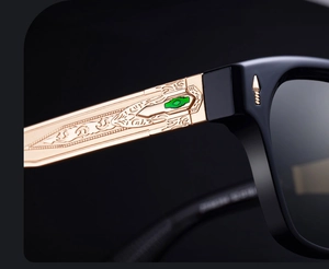 Macro detail of gold baroque embossed sunglasses temple with green inset and black frame