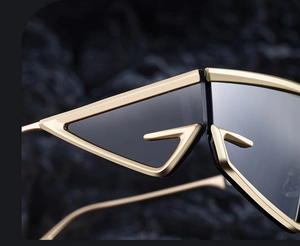 Macro shot of gold G-shaped geometric frame sunglasses with dark lenses on black rock