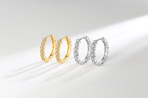 Détail macro de boucles d'oreilles huggies dorées et argentées serties de zircons