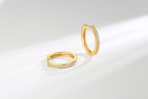 Detailed close-up of golden hoop earrings with clear pavé zircon stones on white background