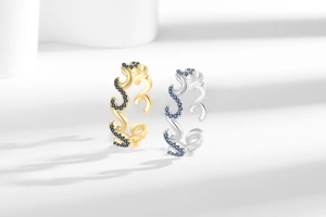 Detailed view of wave-shaped rings with blue zircons in gold and silver finishes