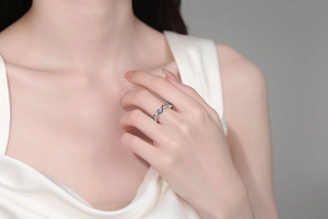 Close-up of wavy silver-tone ring with blue zircons worn by a model in white satin