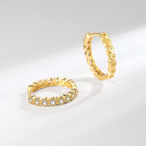 Boucles d'oreilles créoles dorées élégantes avec zircons blancs sur fond minimaliste