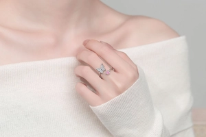 Gros plan d'une bague papillon en argent avec une pierre rose sur le doigt d'une femme