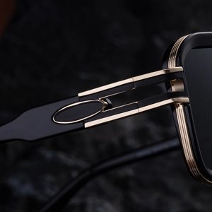 Close-up of black square sunglasses with gold metal hinges and oval temple accents