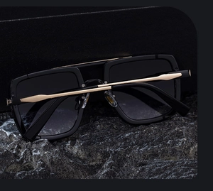 Detail view of square frame sunglasses with golden metal temples on dark rock background