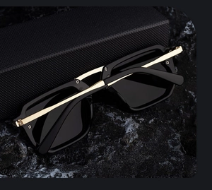 Detail view of square sunglasses with gold metal temples on a dark stone background