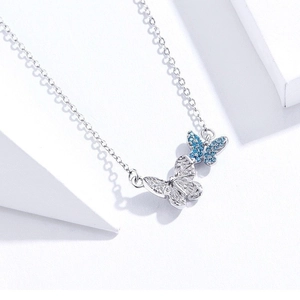 Silver double butterfly necklace with blue zircon pendant on white geometric background