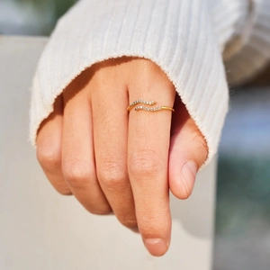 Minimalist gold wave ring with sparkling zircons shown on hand with a white sweater
