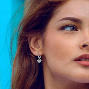 Elegant silver heart drop hoop earrings with sparkling stones worn by a model