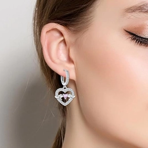 Silver heart earrings with pink zircon and wings shown on a model side view