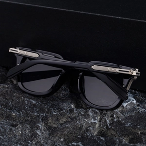 Close-up of square sunglasses with silver metal hinge details on black stone base
