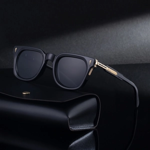 Square black sunglasses with thick frames and gold metal accents on a leather case