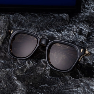 Classic square frame sunglasses with amber lenses on black volcanic rock background