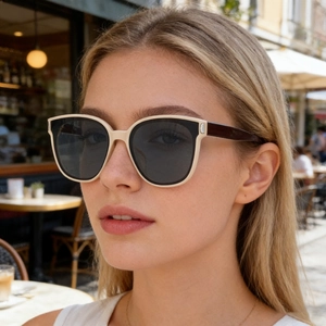 Detailed view of square cream frames with dark lenses worn in sunny outdoor setting