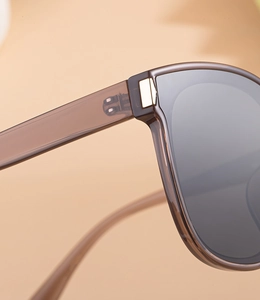 Close-up of golden metal hinge and translucent brown frame on square sunglasses