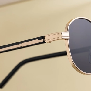 Detail of golden metal hinge and sleek black-gold temple on oval luxury sunglasses