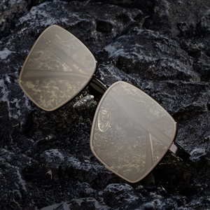 Modern square polarized sunglasses with black gold frame on a dark volcanic rock background