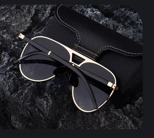 Detail of aviator sunglasses with gold metal frame on dark rock with leather case