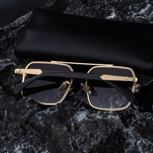 Macro shot of gold metal frame sunglasses with engraved temples on a dark rock background