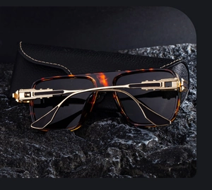 Detail of square frame sunglasses with golden hollowed metal temples on a black rock base