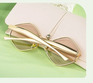 Détail de lunettes de soleil polygonales dorées posées sur un étui en cuir rose