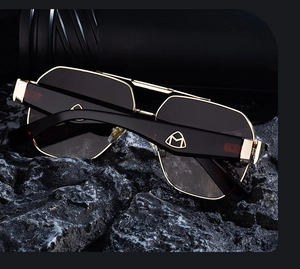 Detail der Goldmetall-Sonnenbrille mit M-Logo am schwarzen Bügel und dunklen Gläsern