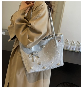Detail of silver gray tote bag with pearl accents and a sparkling bow charm on shoulder strap