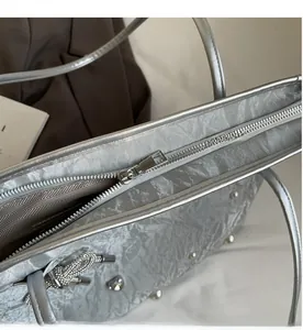 Detail view of smooth silver metal zipper and pearled bow charm on silver tote bag