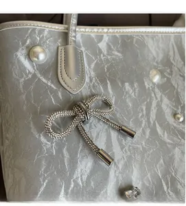 Detailed close-up of crinkled silver tote bag with pearl and rhinestone bow charm decoration