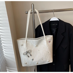 Detail view of cream tote bag with pearl accents and sparkling diamond bow decoration