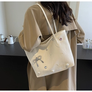 Detail of cream tote bag featuring pearl accents and a decorative bow on the side