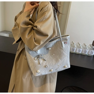 Silver tote bag with bow and pearl details shown on model in a brown trench coat