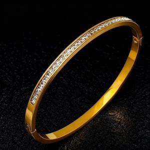 Macro detail of polished gold-plated titanium bangle with square-cut cubic zirconia inlay