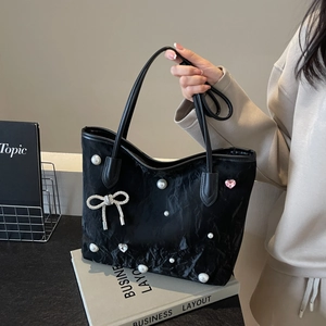 Black tote bag with pearls and bow detail held by a model in a minimalist urban setting