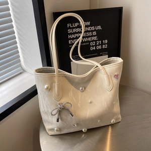 Chic off-white textured tote bag with pearls and bow charm on a round metal display