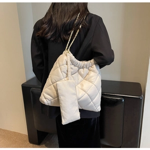 Detail of a beige quilted bucket bag with chain strap and matching coin purse on a model