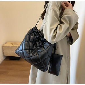Detail of black quilted bucket bag featuring gold chain strap and mini side pouch