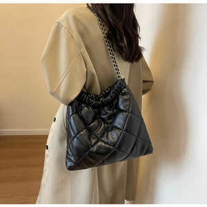 Detail of black quilted chain shoulder bag worn with a beige trench coat for work
