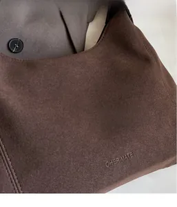 Gros plan du logo CHERIMATE gravé sur le sac à bandoulière en daim marron foncé