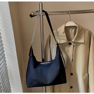 Détail du sac à bandoulière noir avec chaîne argentée et fermeture éclair sur fond beige