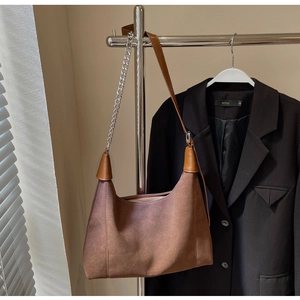 Détail du sac hobo en daim marron avec bandoulière en chaîne métallique et logo sur tissu vintage