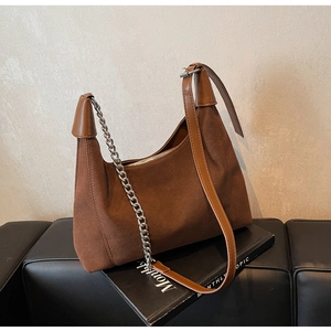 Détail du sac demi-lune en daim marron avec chaîne argentée et poignée en cuir sur un banc