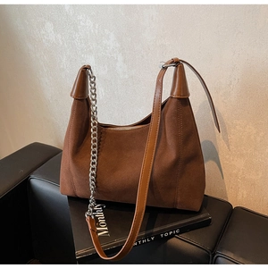 Gros plan du sac bandoulière en daim marron montrant la chaîne argentée et la texture