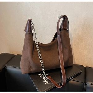 Détail d'un sac porté épaule en daim marron foncé avec chaîne argentée sur des livres